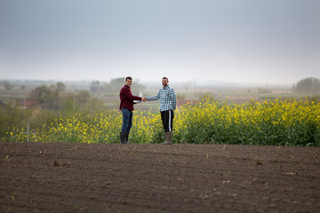 Farmers shaking hands in rapeseed field