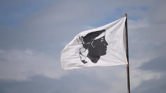 Corsican flag waving in front of a mountain on the Sentier des Douaniers (Custom Officers Route), a famous coastal path for hikers, Corsica, France