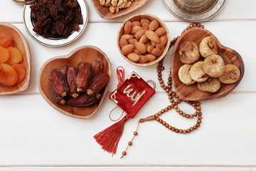 Ramadan iftar party concept. Islamic holy book Quran and rosary beads with delicious dates, dried figs, dried apricots, walnuts, almonds, raisins on bamboo plates on a white wooden table background.