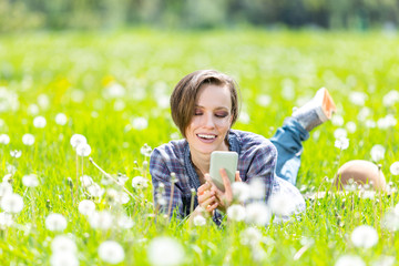 Beautiful woman lying  on a sunny meadow with dandelin and talking on the phone