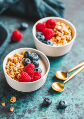 Vegetarian breakfast, bowls with organic granola, fresh raspberries and blueberries and coconut yoghurt.
