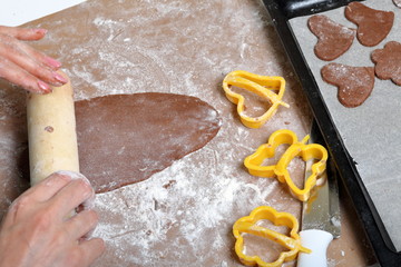 A woman is holding a gingerbread blank. The working surface is in flour, the tools lie next to it. Cooking gingerbread.