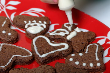 Baked gingerbread cookies are lying on a plate. A woman squeezes the icing from the tube, decorating cookies. Some are decorated with white icing. Cooking gingerbread.