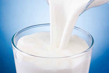 Pouring fresh milk into glass on a blue background