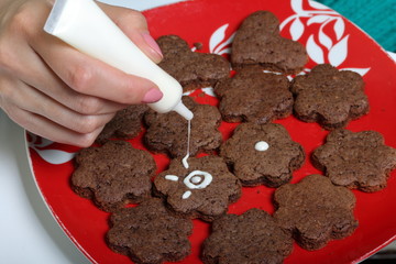 Baked gingerbread cookies are lying on a plate. A woman squeezes the icing from the tube, decorating cookies. Some are decorated with white icing. Cooking gingerbread.