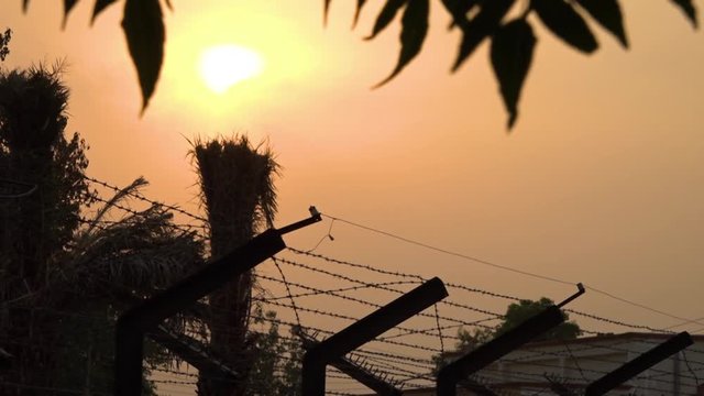 Low angle shot of the sun setting in vibrant orange sky above bard wire fencing at the border between India and Pakistan