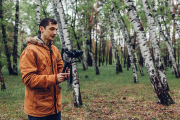 Naklejka premium Videographer filming spring forest. Man using steadicam and camera to make footage. Video shoot