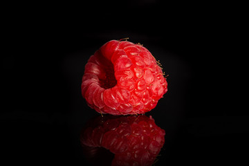 One whole fresh red raspberry isolated on black glass
