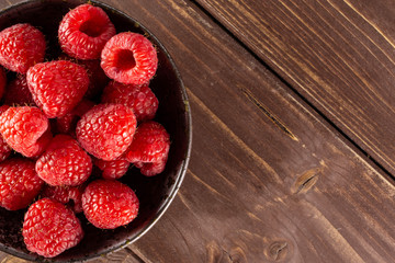 Lot of whole fresh red raspberry on grey ceramic plate flatlay on brown wood