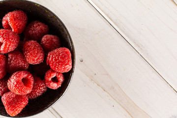 Lot of whole fresh red raspberry on grey ceramic plate flatlay on white wood