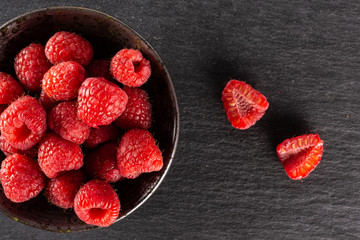 Group of lot of whole two halves of fresh red raspberry on grey ceramic plate flatlay on grey stone