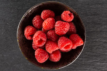 Lot of whole fresh red raspberry on grey ceramic plate flatlay on grey stone