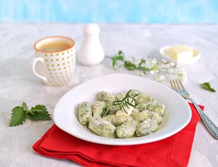 Gnocchi or dumplings with nettle or spinach on a white plate on a light gray background. Served with butter and parmesan cheese. Italian food. Selective focus