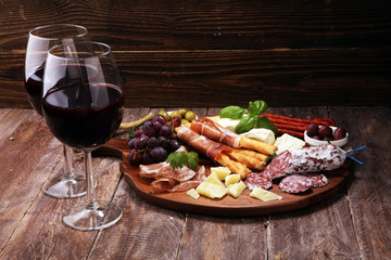 antipasto various appetizer. Cutting board with prosciutto, salami, cheese, bread and olives on dark wooden background