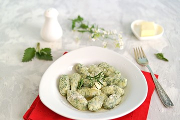 Gnocchi or dumplings with nettle or spinach on a white plate on a light gray background. Served with butter and parmesan cheese. Italian food. Selective focus