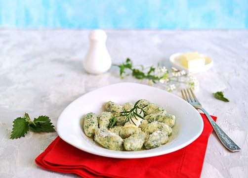 Gnocchi or dumplings with nettle or spinach on a white plate on a light gray background. Served with butter and parmesan cheese. Italian food. Selective focus
