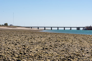 Fototapeta premium Beach with small stones with pier marking the horizon, sky and blue sea.