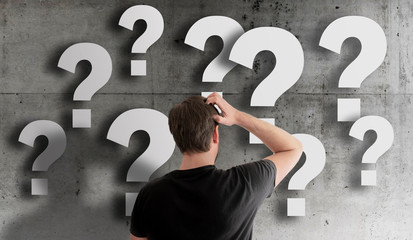 rear view of puzzled man scratching his head against concrete wall filled with question marks