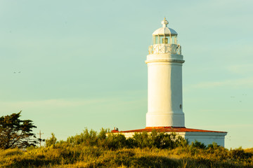 View of lighthouse, colors: green, red, yellow, white and sky with few clouds.