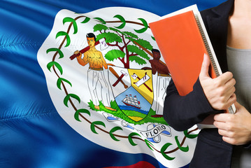 Learning Belizean language concept. Young woman standing with the Belize flag in the background. Teacher holding books, orange blank book cover.