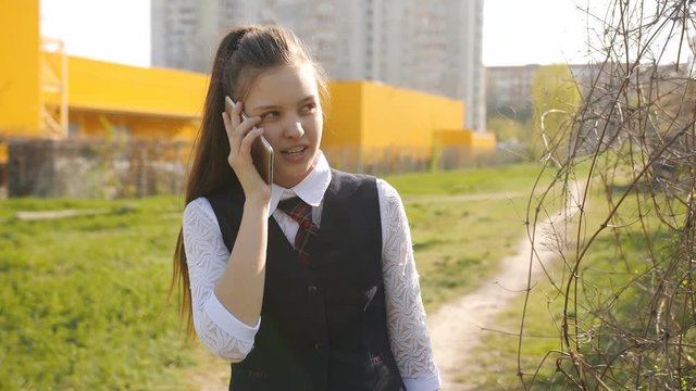 Schoolgirl comes home from school. Girl teenager talks to his mom on the phone on the way home.
