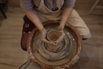 Potter working on potters wheel making ceramic pot from clay in pottery workshop
