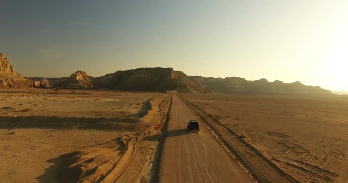 An aerial crane shot of an black offroad car moving middle in great desert An 4WD black offroad car moving along sandy road middle in great desert with mountains during golden hour