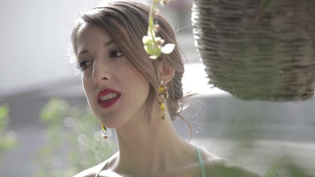 Giovane bella ragazza in vacanza con rossetto, maglia azzurra, si rinfresca dal caldo con un ventaglio bianco, affacciata dal balcone di casa.