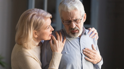 Grey haired man touching chest, having heart attack, woman supporting