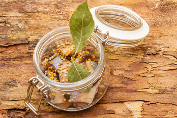 Slices of herring with spices in a glass jar.