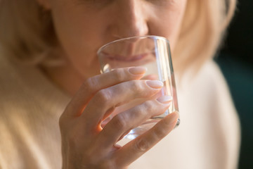 Close up mature woman drinking pure water, holding glass in hand