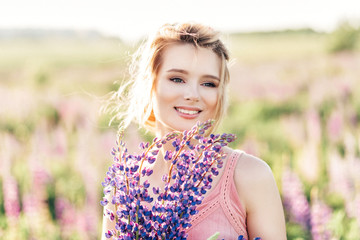 Beautiful girl in a field of purple lupines in a summer day
