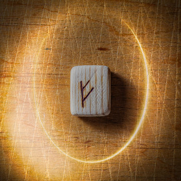 Fehu. Handmade scandinavian wooden runes on a wooden vintage background in a circle of light. Concept of fortune telling and prediction of the future.