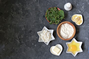 Ingredients for cooking gnocchi or dumplings with nettle on a dark gray concrete background: ricotta cheese, fresh nettle, egg, wheat flour, parmesan cheese, butter, salt. Top view, copy space.