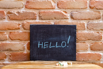 Black board with the word HELLO! drown by hand on wooden table on brick wall background.