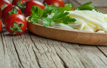 string cheese in bamboo bowl with cherry tomatoes on wooden background. Cecil or chivil cheese, turkish food breakfast cheese concept