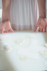Obraz na płótnie Canvas photo women's dress and hands dipped in water in a natural milk bath with foam and flowers
