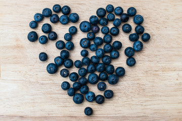 Blueberries in the shape of a heart lying on a wooden background. Blue berries, healthy food on dark table mockup, berry for smoothie on vintage rustic country board. Top view.