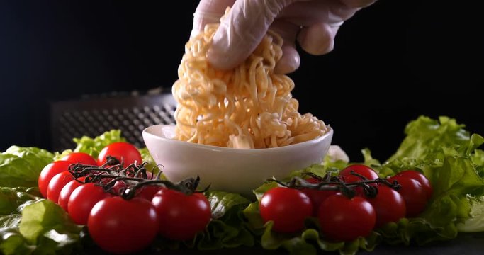 On a black background, vegetables and noodles on a wooden table, the whole dish is rubbed on top with parmesan cheese and mixed noodles. Concept of: Grater, Cheese, Noodles, Cherie Tomatoes, Salad.