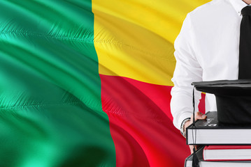 Successful Beninese student education concept. Holding books and graduation cap over Benin flag background.