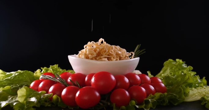 On a black background, vegetables and noodles on a wooden table, the whole dish is rubbed on top with parmesan cheese and mixed noodles. Concept of: Grater, Cheese, Noodles, Cherie Tomatoes, Salad.