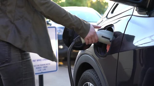 Young woman unplugs disconnects charging cable electric vehicle parking only, holding power charger cable, charging port, EV sustainable future at sunset view