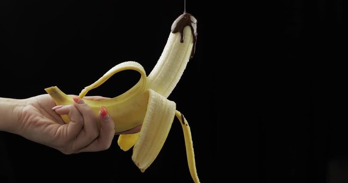 Pouring a banana with melted dark chocolate syrup. Black background