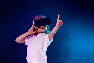 Girl 7 y.o. experiencing VR headset game on colorful background. Child pointing finger while using a gaming gadget for virtual reality. Futuristic goggles at young age. Virtual technology