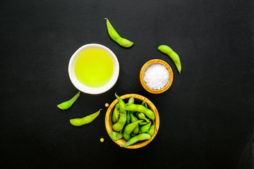 Fresh edamame and oil on black background top view