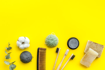 eco friendly bamboo tooth brush and carbon toothpaste, comb, organic soap on yellow background top view space for text