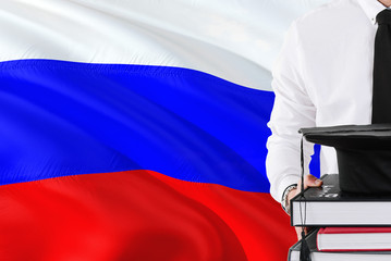 Successful Russian student education concept. Holding books and graduation cap over Russia flag background.