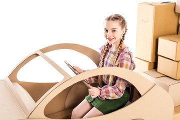 Obraz premium happy kid looking at camera and holding steering wheel while playing with cardboard car Isolated On White