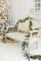 Stylish Christmas light interior with a soft armchair or sofa decorated with garland. Comfort home. Christmas tree with presents underneath in living room
