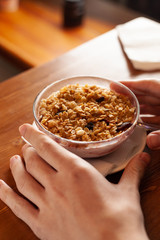 Hands holding a bowl of whole grain muesli and raisins for breakfast